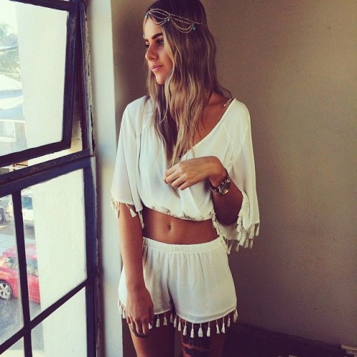 a white boho outfit with a crop top with bell sleeves and shorts wihth tassels plus a boho headpiece