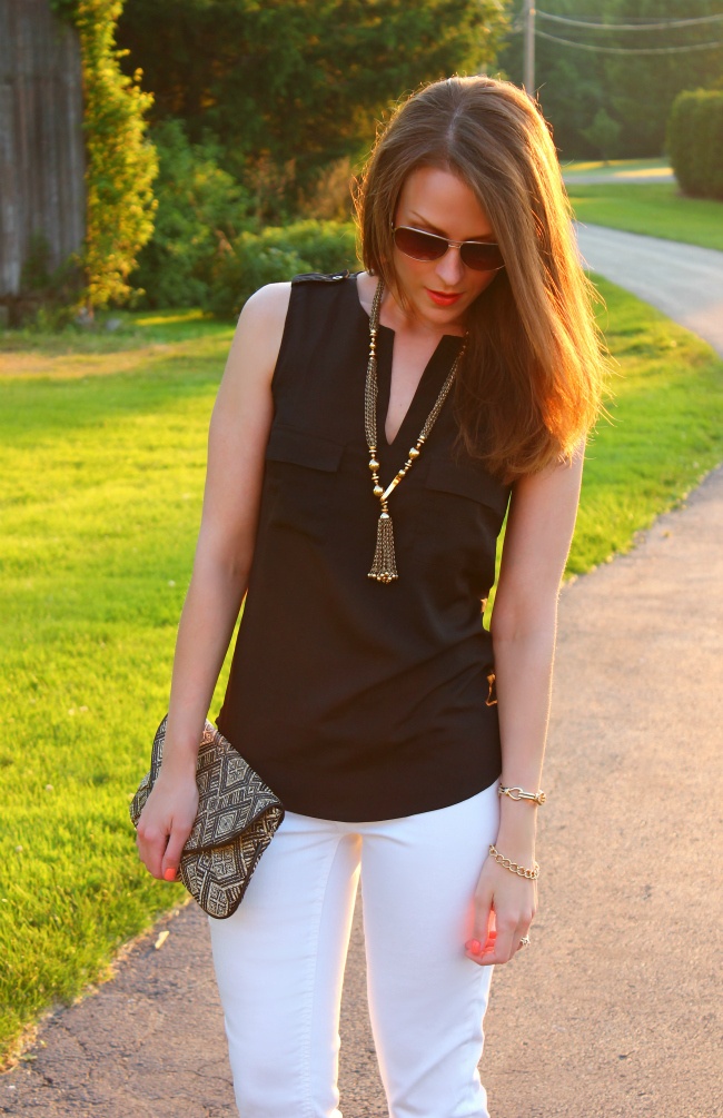 a black sleeveless shirt, white jeans, a statement necklace and an embellished clutch