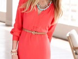 a coral knee dress with long sleeves, a V-neckline, layered necklaces, a belt and stacked bracelets