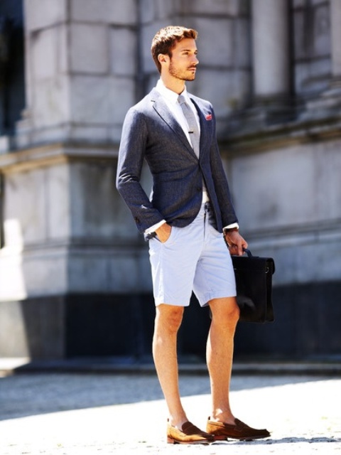 a summer work look with light blue shorts, a white shirt, a grey tie, a navy blazer, brown moccasins and a black bag