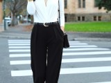 a white blouse with a deep cut is compensated with black widelegs pants, a black bag and black heels